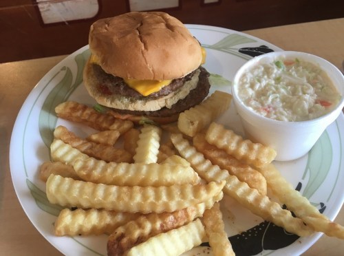 A plate with a cheeseburger, crinkle-cut fries, and a cup of coleslaw.