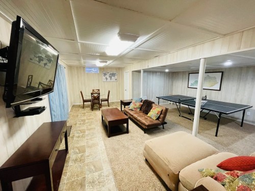 A cozy basement living area with a sofa, coffee table, TV, dining table, and a ping pong table.