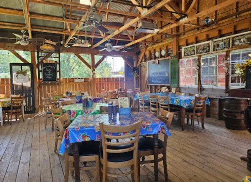 A rustic dining area with wooden tables, colorful tablecloths, and a cozy, open atmosphere.