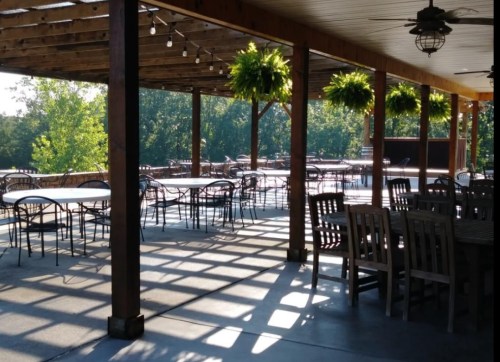 Outdoor dining area with wooden beams, hanging plants, and empty tables under a sunny sky.