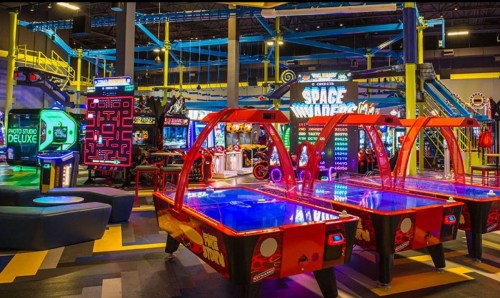 Bright arcade with red air hockey tables, classic games like Space Invaders, and colorful lighting in a fun atmosphere.