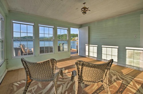 Cozy sunroom with two chairs, large windows, and a view of the lake. Light green walls and natural light create a serene atmosphere.