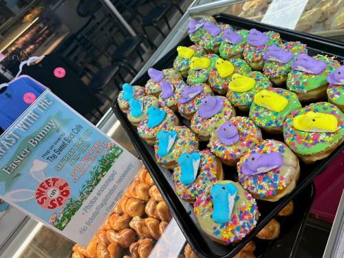 A tray of colorful donuts topped with sprinkles and marshmallow bunnies, displayed in a bakery.