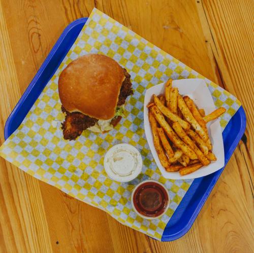 A tray with a crispy chicken sandwich, fries, and dipping sauces on a checkered paper.