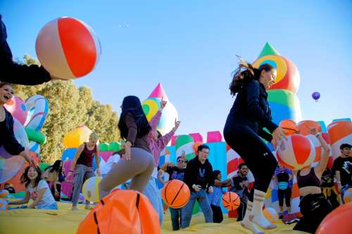 A lively scene of people playing with colorful beach balls in a vibrant inflatable playground.