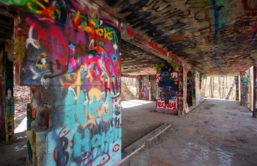 Vibrant graffiti covers the walls of an abandoned building, with sunlight streaming through open spaces.
