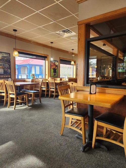 Interior of a restaurant featuring wooden tables and chairs, large windows, and a cozy atmosphere.