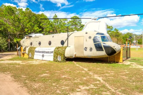 A decommissioned helicopter displayed on a grassy area, with a banner in front and trees in the background.