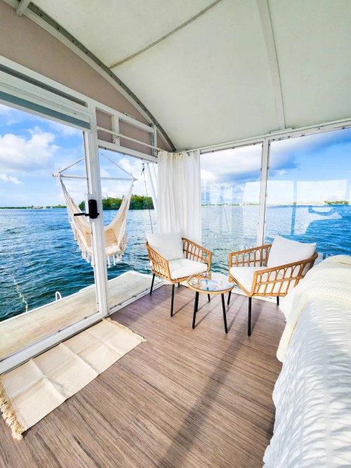 Cozy waterfront seating area with two chairs, a small table, and a hammock, overlooking a serene lake view.