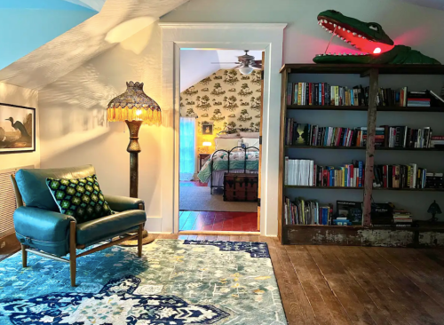 Cozy attic space with a blue armchair, patterned rug, bookshelf, and a whimsical alligator decoration with glowing eyes.