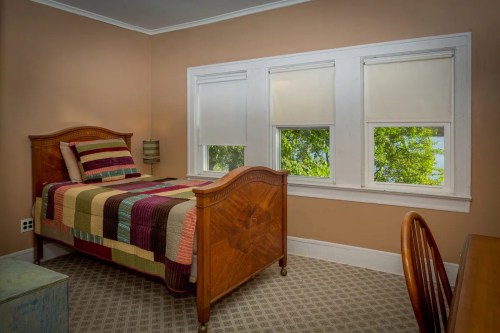 Cozy bedroom with a wooden bed, colorful quilt, and large windows overlooking greenery.