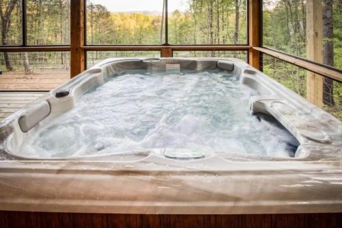 A hot tub filled with water, set in a wooden cabin surrounded by trees and a scenic view outside.