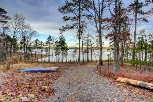 A serene lakeside view with colorful kayaks on a gravel path surrounded by trees and autumn foliage.