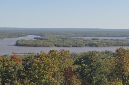 A scenic view of a river winding through lush green forests under a clear blue sky.