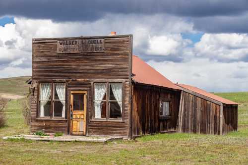 A weathered wooden building with a slanted roof, featuring large windows and a sign that reads "Walker & Odell Homestead Dealers."