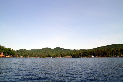 A serene lake surrounded by green hills and trees under a clear blue sky.