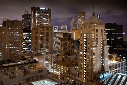 A nighttime cityscape featuring illuminated skyscrapers and a mix of modern and historic architecture.