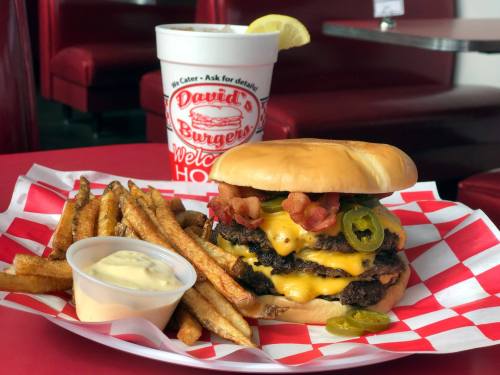 A juicy cheeseburger with bacon and jalapeños, served with fries and a drink in a diner setting.