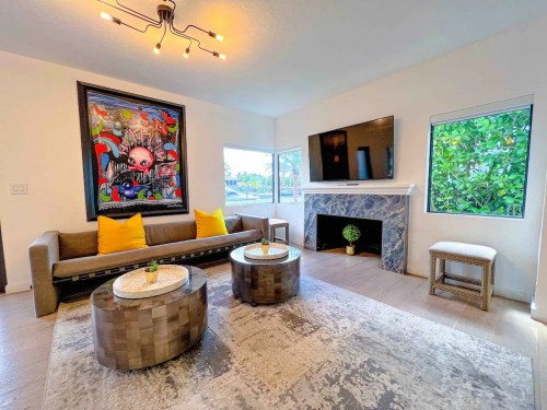 Modern living room with a colorful artwork, a gray sofa, two round coffee tables, and large windows.