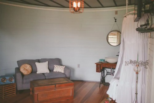 Cozy interior of a circular room featuring a gray sofa, wooden chest, mirror, and decorative elements.