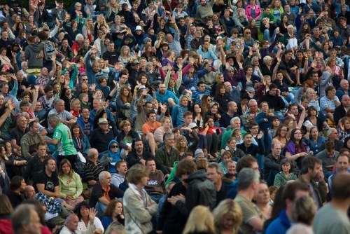 A large crowd of people gathered outdoors, many with hands raised, enjoying an event or performance.
