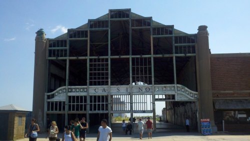 A large, abandoned casino building with a distinctive architectural design, surrounded by people walking outside.