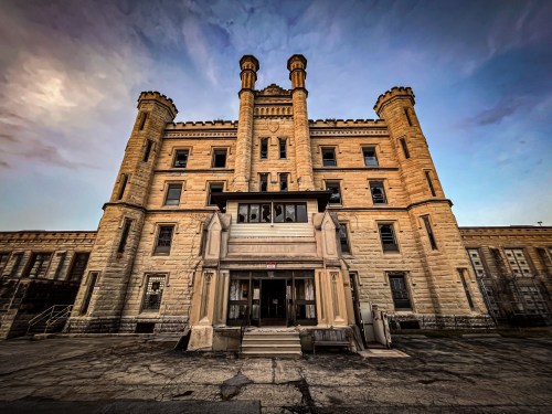 Historic stone building with towers, featuring a central entrance and a cloudy sky in the background.