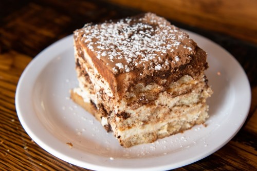 A slice of layered chocolate dessert topped with powdered sugar on a white plate.