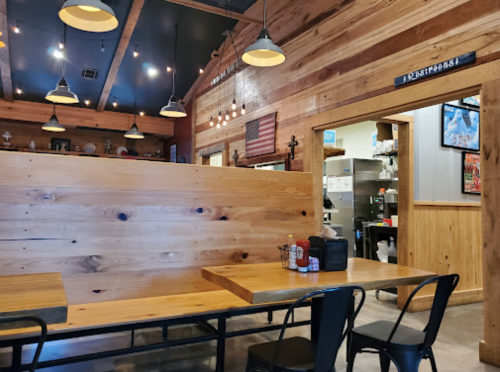 Cozy wooden interior of a restaurant with tables, warm lighting, and an open kitchen visible in the background.