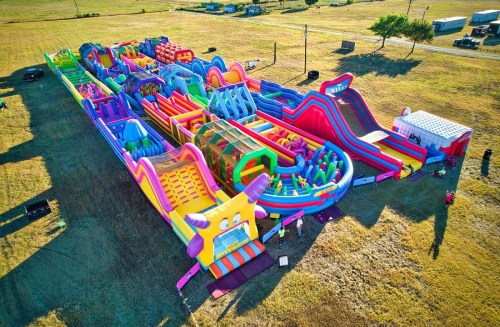Aerial view of a large, colorful inflatable obstacle course set in an open field.