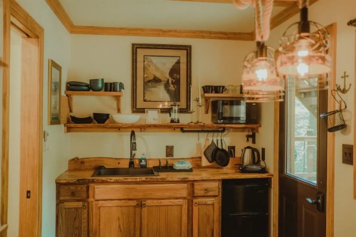 Cozy kitchen with wooden shelves, sink, microwave, and black appliances, featuring warm lighting and rustic decor.