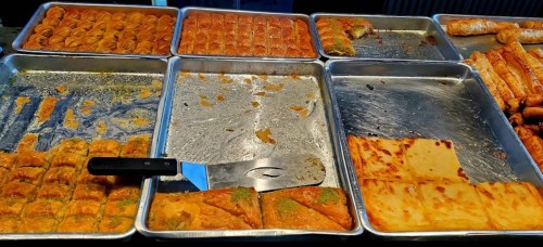 A variety of pastries displayed on trays, including baklava and other sweet treats, in a vibrant setting.