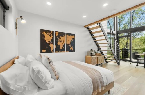 Cozy bedroom with a large bed, world map art, and a staircase leading to a bright, modern living area.