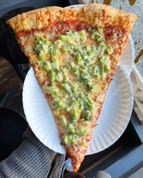 A large slice of pizza topped with cheese, broccoli, and green peppers on a paper plate.