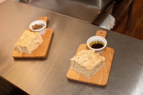 Two wooden boards with slices of bread and small bowls of olive oil and seasoning on a stainless steel surface.