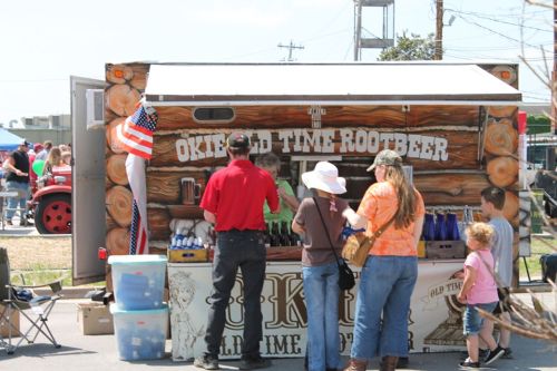 A root beer stand with a wooden design, people ordering drinks, and an American flag displayed nearby.