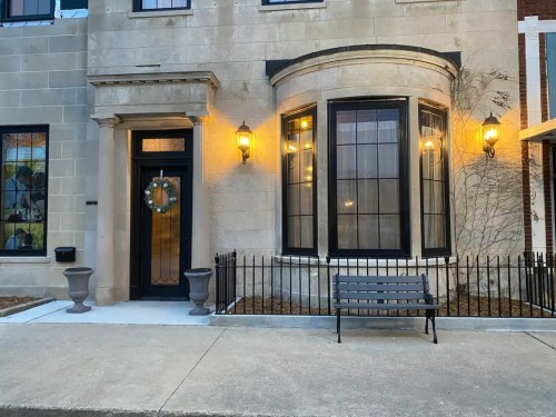 A charming building entrance with large windows, a decorative wreath, and a bench in front, illuminated by warm lights.