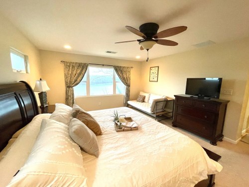 Cozy bedroom with a large bed, window, TV, and seating area, featuring warm colors and decorative curtains.