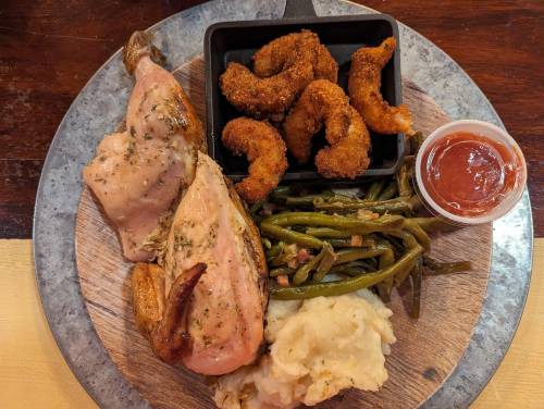 A plate featuring roasted chicken, green beans, mashed potatoes, fried shrimp, and a side of dipping sauce.