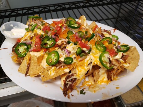 A plate of nachos topped with cheese, jalapeños, diced tomatoes, onions, and a side of sour cream.