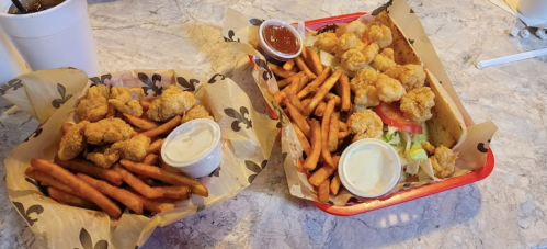 Two baskets of fried food: one with chicken and fries, the other with shrimp, fries, and dipping sauces on a table.