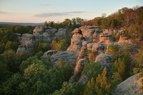 Rock formations surrounded by lush greenery under a colorful sunset sky.
