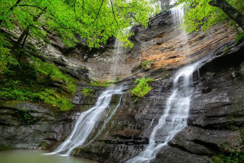 A serene waterfall cascading down rocky cliffs, surrounded by lush green foliage and a tranquil pool below.