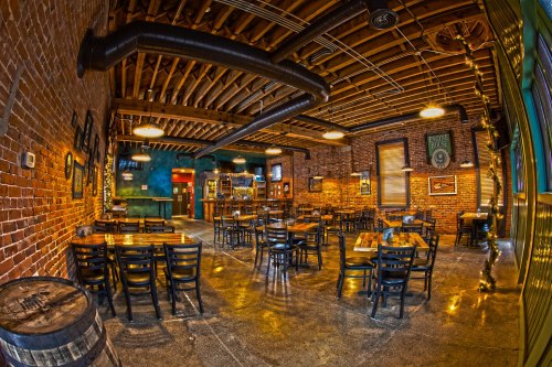 Interior of a rustic restaurant with exposed brick walls, wooden tables, and a bar area, featuring warm lighting.