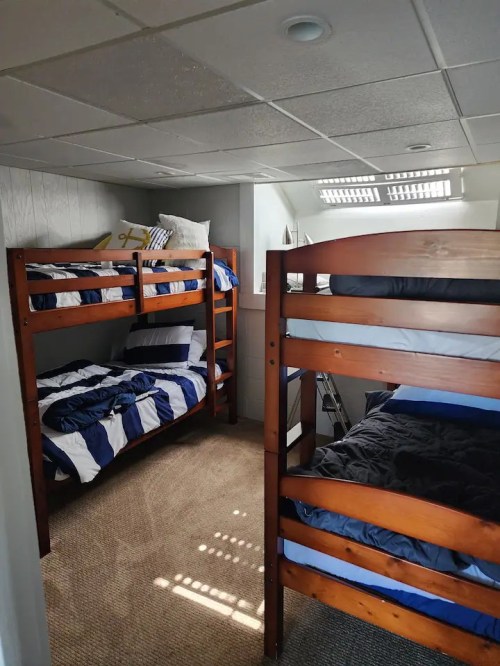 A cozy room with two sets of wooden bunk beds, featuring blue and white bedding, and carpeted flooring.