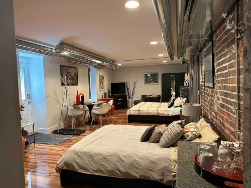 A cozy studio apartment featuring two beds, a dining area, and exposed brick walls with modern decor.