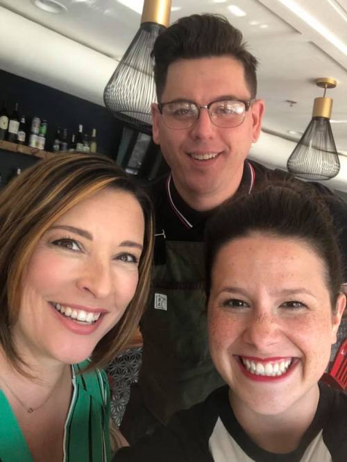 Three smiling individuals pose for a selfie in a stylish restaurant setting.