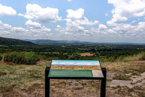 A scenic view from a lookout point with a sign displaying information about the landscape and surrounding area.