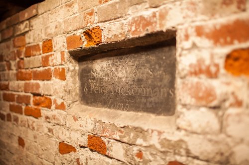 A weathered stone plaque on a brick wall, inscribed with "Samuel Watts & Peter Dickerman's Tomb."