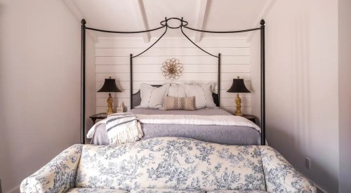 A cozy bedroom featuring a four-poster bed, decorative wall art, and a floral-patterned sofa in soft colors.